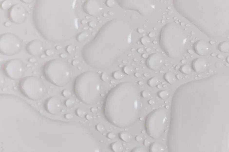 Closeup top view of wet plain white background of droplet with translucent clean still water drops of different shapes and sizes