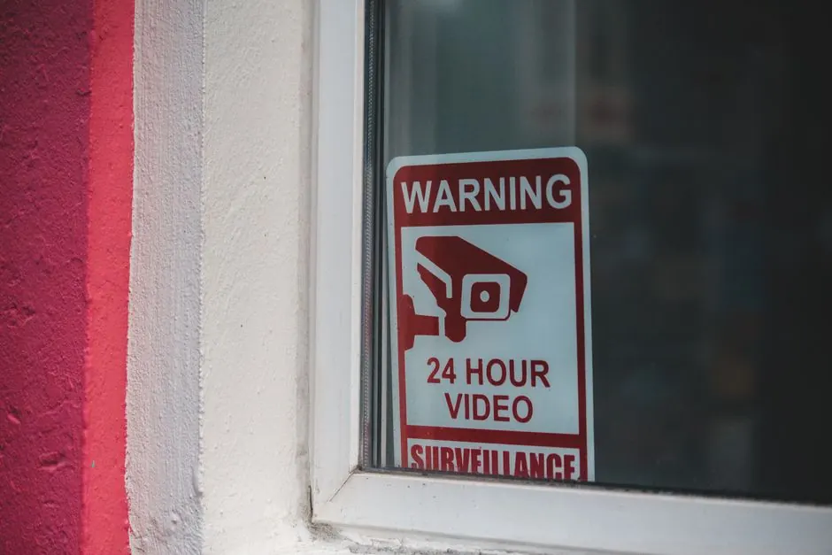 Red warning sign of video surveillance placed behind window of building in daytime